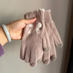 Détail de gants en tricot rose avec nœud en peluche blanc et bouts tactiles gris