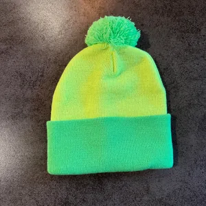 Top view of bicolor knit beanie with pompom in neon yellow and green on stone background