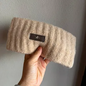 Detail of beige ribbed knit headband featuring a premium leather logo patch and soft texture