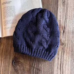 Dettaglio di un berretto in maglia a trecce blu navy con motivi a treccia su legno
