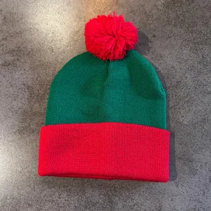 Close-up of red and green knit beanie with festive pompom and thick ribbed texture