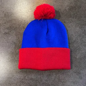 Detail of blue and red knit beanie featuring a ribbed texture and large red pom-pom