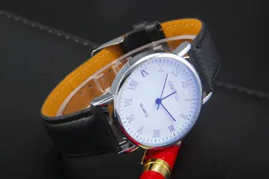 Close-up of Geneva quartz watch with Roman numerals and black leather strap next to a pen
