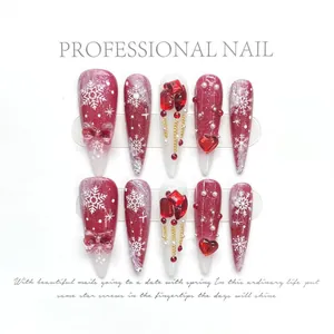 Close-up of handmade press-on nails with red bows, snow patterns and pearls