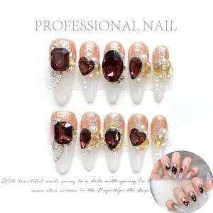 Détail de faux ongles de luxe avec forme stiletto, perles et pierres rouges
