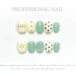 Détail de faux ongles faits main menthe et crème avec perles et rivets dorés décoratifs