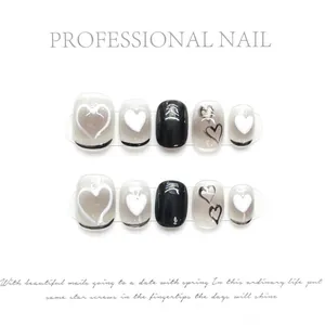 Primer plano de uñas postizas hechas a mano con diseños de corazones negros, blancos y brillo