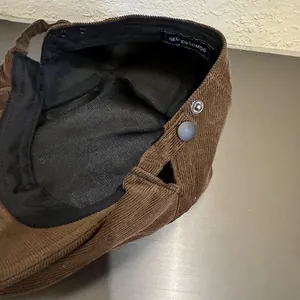 Détail de la casquette en velours côtelé marron avec bouton-pression en métal et étiquette