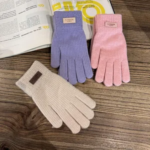 Drie paar gebreide handschoenen in lila, roze en crème op een houten achtergrond