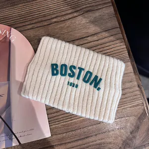 Détail de bandeau en tricot blanc crème avec lettrage Boston vert sur une table en bois