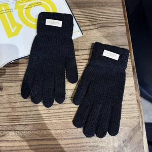 Detail van zwarte gebreide handschoenen met wit geweven label op houten tafel