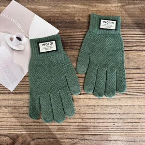 Detail of dark green knit gloves with warm label on a textured wooden background