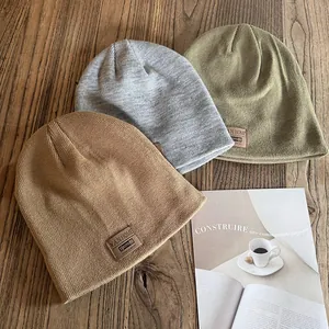 Three knitted beanie hats in khaki grey and green with leather patch on wooden desk