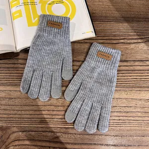 Detail of dark grey knit gloves with brown leather fashion tag and ribbed warm cuffs