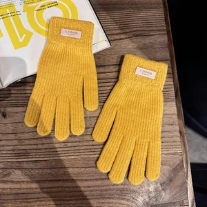 Detail van felgele gebreide handschoenen met ribbeltextuur en label op houten tafel