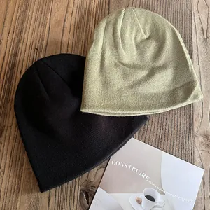 Close-up of black and olive green knitted beanies on a warm wooden surface with decor