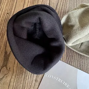 Detail view of ribbed knit beanies in black and olive green on a natural wooden background