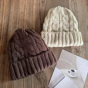Detail von grob gestrickten Beanies in Braun und Beige auf rustikalem Holzhintergrund