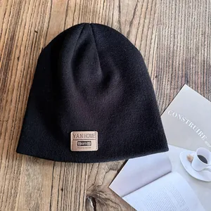 Detail of black knit beanie with a vintage brown leather patch on a wood surface