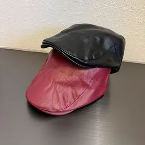 Detailed view of two faux leather beret hats in black and burgundy with smooth texture