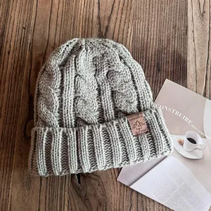 Detailaufnahme einer hellgrauen Strickmütze mit Lederpatch auf rustikalem Holzhintergrund