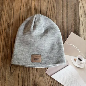 Close-up of grey knit beanie with premium brown leather label on wooden table