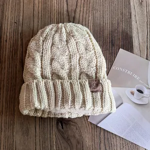 Nahaufnahme der beigen Strickmütze mit warmem Fleecefutter und Lederaufnäher auf Holz