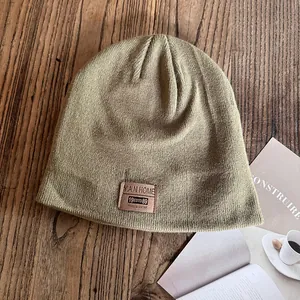 Detail of mustard yellow knit beanie with leather brand patch on wood table