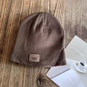 Close-up of a dark brown knitted beanie with a leather logo patch on a wooden table
