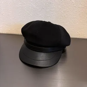 Detail of black newsboy hat featuring textured fabric body and faux leather brim accent