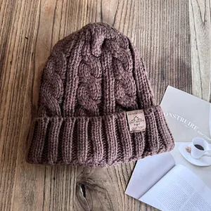 Detailansicht der kaffeebraunen Strickmütze mit Zopfmuster und dekorativem Lederpatch