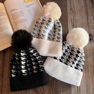 Three houndstooth knit beanies with fluffy pom poms on vintage wood background