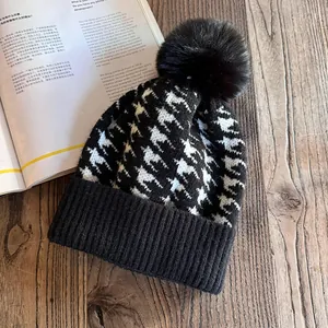 Detail of black and white houndstooth knit beanie with large faux fur pompom on wood surface