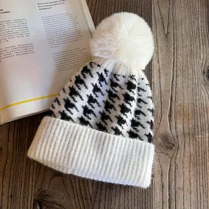 Close-up of houndstooth knit beanie with a fluffy faux fur pom-pom on wooden background
