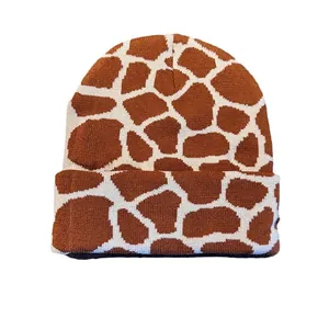 Knit beanie hat featuring brown and beige giraffe animal pattern with folded cuff