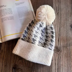 Detail of winter houndstooth knit beanie featuring a cream faux fur pom-pom on wood