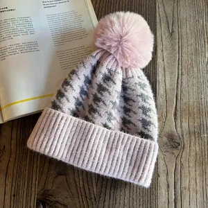 Detailed close-up of pink and grey houndstooth knit beanie with a large fluffy pom-pom