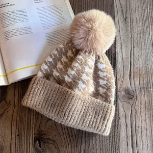 Detail of beige houndstooth knitted hat with a large faux fur pompom on wood