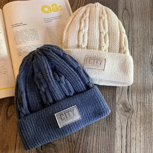 Detail of cable knit beanies in cream and navy blue showing textured weave and fabric labels