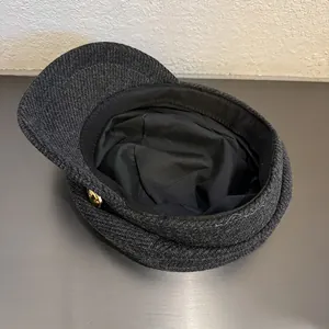 Detail showing heavy wool texture, gold metal button, and black lining of the grey newsboy cap