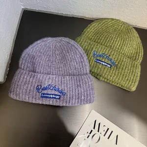 Detailed view of two ribbed knit beanies in purple and green with custom embroidery