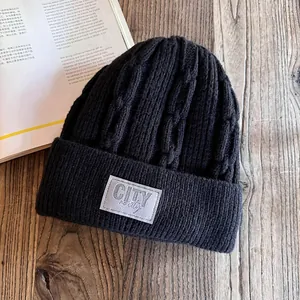 Detail of black cable knit beanie with fleece lining and City woven patch on wooden background