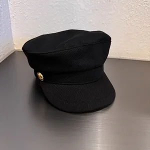 Side view of black wool newsboy hat with a textured finish and gold metal button