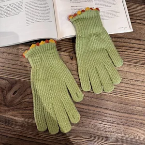 Detail of green knitted gloves featuring colorful pom-pom trim on a cozy wooden background