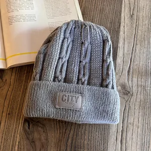 Detail of grey cable-knit beanie with a rectangular woven patch on a vintage wood desk