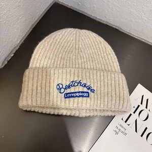 Close-up of ribbed knit texture on a beige beanie with blue embroidered logo and lettering