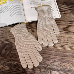 Detailed texture of beige knitted gloves with decorative green wavy borders on wood surface