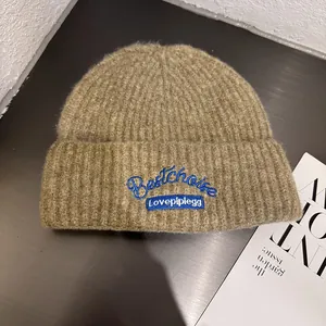 Detail of tan knit beanie featuring blue embroidery on a soft textured wool blend fabric