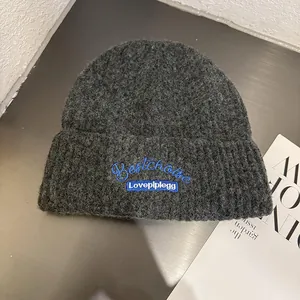 Detail view of dark grey knitted beanie with blue embroidery and chunky texture finish