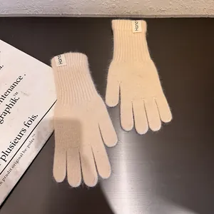 Detailaufnahme beiger Strickhandschuhe mit weißem Hand-Label auf einem braunen Tisch